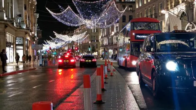 A London street at night with holiday lights and buses.