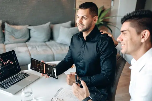 Two businessmen analyzing stock market data on a tablet in a modern office setting.