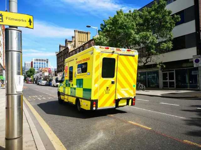 A London ambulance driving along a city street.