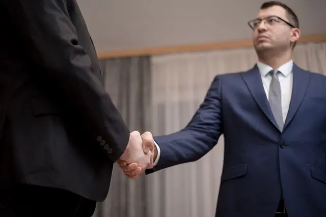 Two businessmen in formal attire shaking hands during a meeting.